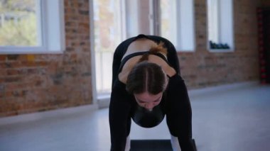 Bir kadın esneme ve pilates yapıyor. Parlak bir stüdyoda esneyen ve dengeyi bulan zarif bir kadın pozu. Gökyüzüne uzanan bir kadın, içindeki gücü yoga akışında bulur. Siyah giysi, odaklanmış ifade