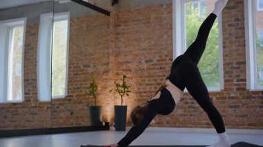 Bir kadın esneme ve pilates yapıyor. Parlak bir stüdyoda esneyen ve dengeyi bulan zarif bir kadın pozu. Gökyüzüne uzanan bir kadın, içindeki gücü yoga akışında bulur. Siyah giysi, odaklanmış ifade