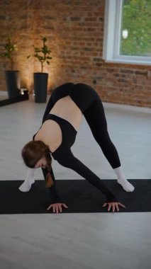 Dikey. Bir kadın stüdyoda esneme hareketleri yapıyor ve pilates yapıyor. Parlak bir stüdyoda esneyen ve dengeyi bulan zarif bir kadın pozu. Gökyüzüne uzanan bir kadın, içindeki gücü yoga akışında bulur. Siyah elbise.,