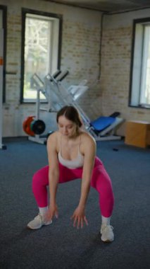 Dikey. Beyaz bluzlu ve pembe taytlı bir kadın spor salonunda spor yapıyor, pilates yapıyor ve esniyor. Bir kız spor salonunda spor yapıyor..