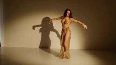 Güzel genç bir kadın göbek dansı yapıyor. Altın elbiseli bir kadın dansçının silueti. Doğulu göbek dansı.