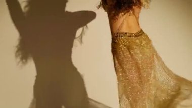 Güzel genç bir kadın göbek dansı yapıyor. Altın elbiseli bir kadın dansçının silueti. Doğulu göbek dansı.