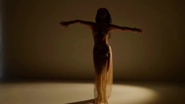 Güzel genç bir kadın göbek dansı yapıyor. Altın elbiseli bir kadın dansçının silueti. Doğulu göbek dansı.