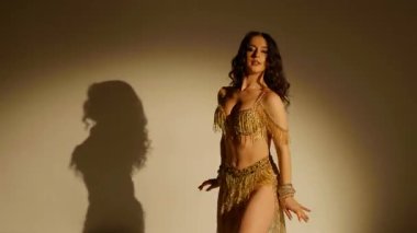 Güzel genç bir kadın göbek dansı yapıyor. Altın elbiseli bir kadın dansçının silueti. Doğulu göbek dansı.