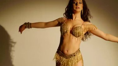 Güzel genç bir kadın göbek dansı yapıyor. Altın elbiseli bir kadın dansçının silueti. Doğulu göbek dansı.