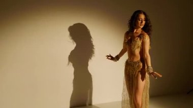 Güzel genç bir kadın göbek dansı yapıyor. Altın elbiseli bir kadın dansçının silueti. Doğulu göbek dansı.