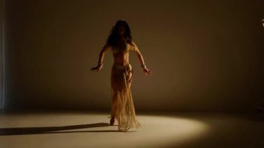 Güzel genç bir kadın göbek dansı yapıyor. Altın elbiseli bir kadın dansçının silueti. Doğulu göbek dansı.