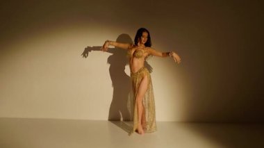 Güzel genç bir kadın göbek dansı yapıyor. Altın elbiseli bir kadın dansçının silueti. Doğulu göbek dansı.