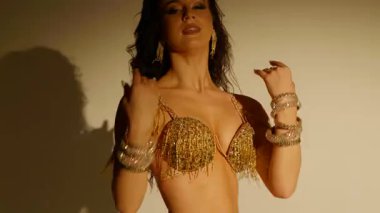 Güzel genç bir kadın göbek dansı yapıyor. Altın elbiseli bir kadın dansçının silueti. Doğulu göbek dansı.