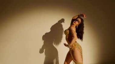 Güzel genç bir kadın göbek dansı yapıyor. Altın elbiseli bir kadın dansçının silueti. Doğulu göbek dansı.