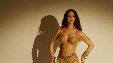 Güzel genç bir kadın göbek dansı yapıyor. Altın elbiseli bir kadın dansçının silueti. Doğulu göbek dansı.