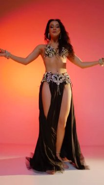 Dikey. Siyah sutyen ve etekle göbek dansı yapan güzel bir genç kadın. Güzel vücutlu narin bir kız doğu dansları yapar. Doğulu göbek dansı.
