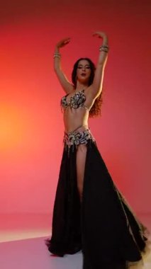 Dikey. Siyah sutyen ve etekle göbek dansı yapan güzel bir genç kadın. Güzel vücutlu narin bir kız doğu dansları yapar. Doğulu göbek dansı.