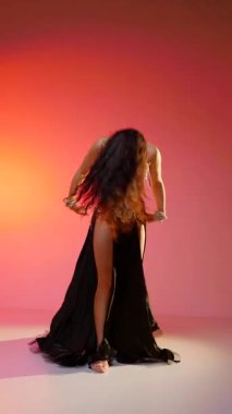 Dikey. Siyah sutyen ve etekle göbek dansı yapan güzel bir genç kadın. Güzel vücutlu narin bir kız doğu dansları yapar. Doğulu göbek dansı.