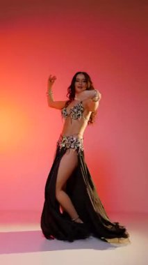 Dikey. Siyah sutyen ve etekle göbek dansı yapan güzel bir genç kadın. Güzel vücutlu narin bir kız doğu dansları yapar. Doğulu göbek dansı.