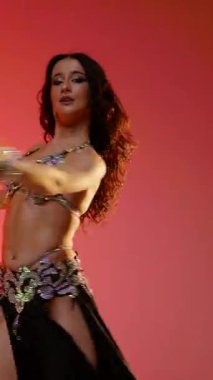 Dikey. Siyah sutyen ve etekle göbek dansı yapan güzel bir genç kadın. Güzel vücutlu narin bir kız doğu dansları yapar. Doğulu göbek dansı.