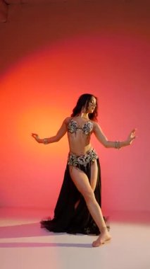 Dikey. Siyah sutyen ve etekle göbek dansı yapan güzel bir genç kadın. Güzel vücutlu narin bir kız doğu dansları yapar. Doğulu göbek dansı.