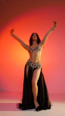 Dikey. Siyah sutyen ve etekle göbek dansı yapan güzel bir genç kadın. Güzel vücutlu narin bir kız doğu dansları yapar. Doğulu göbek dansı.