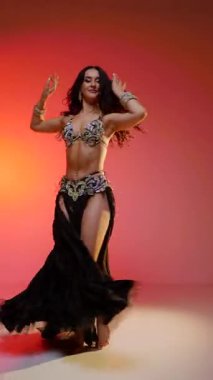 Dikey. Siyah sutyen ve etekle göbek dansı yapan güzel bir genç kadın. Güzel vücutlu narin bir kız doğu dansları yapar. Doğulu göbek dansı.