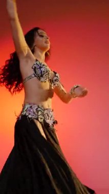 Dikey. Siyah sutyen ve etekle göbek dansı yapan güzel bir genç kadın. Güzel vücutlu narin bir kız doğu dansları yapar. Doğulu göbek dansı.