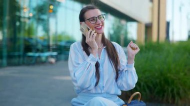Gözlüklü bir iş kadını sokakta bankta otururken telefonla konuşuyor. Zarif ve başarılı bir kadın akıllı telefondan canlı bir iş görüşmesi yapıyor..