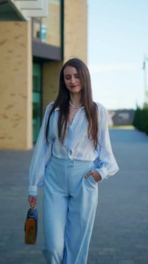 Dikey. Mutlu bir kadın güvenli bir şekilde dolaşır, açık mavi elbisesi güneşin ışınlarını yakalar, adımlarında biraz sofistike bir dokunuş. Açık mavi, çizgili gömlek ve pantolon, şık bir takım.