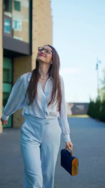 Dikey. Mutlu bir kadın güvenli bir şekilde dolaşır, açık mavi elbisesi güneşin ışınlarını yakalar, adımlarında biraz sofistike bir dokunuş. Açık mavi, çizgili gömlek ve pantolon, şık bir takım.