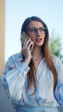 Dikey. Muhabbete dalmış bir iş kadını, gülüşü olumlu bir değiş tokuşa işaret ediyor. Şık ve cana yakın, açık mavi tişörtlü bir kadın, telefonda biriyle iletişim kuruyor..