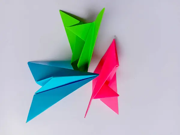 Beyaz arkaplanda mavi, yeşil ve pembe uçak origamisi.