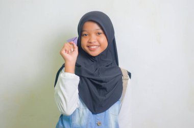 Gülümseyen küçük Müslüman kız beyaz arka planda izole edilmiş origami uçağı ya da kağıt uçak oynuyor..