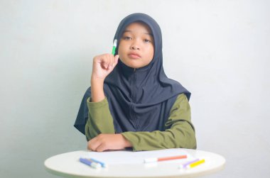 Beyaz arka planda izole edilmiş bir işaret tutarken küçük tatlı bir kız fikir üretiyor. Güzel Asyalı Müslüman kız.