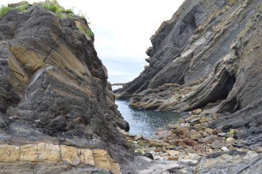 Büyük kahverengi kayalarla çevrili mavi sahil.