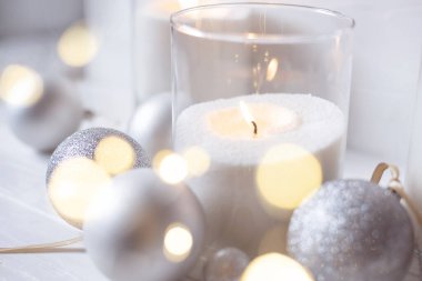 Aydınlık bir arka planda neşeli bokeh ve gümüş toplarla mum yakmak. Tatil kavramı