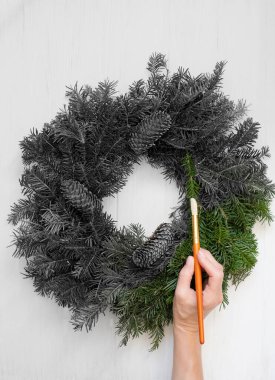 Köknar dallarından oluşan bir Noel çelengi ve renkli bir dünyaya fırça resmi taşıyan bir elin siyah beyaz fotoğrafı. Kavram - dünyayı renklerle boyamak