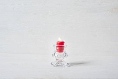 Cam şamdan ve beyaz ahşap zeminde yanan kırmızı mum.