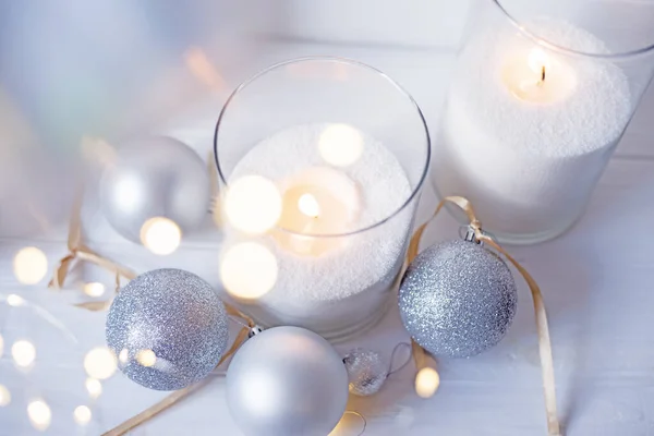 Burning candles with festive bokeh and silver balls on a light background. Holiday concept