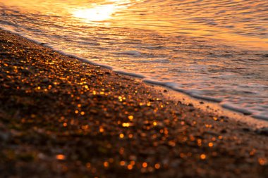   Deniz yüzeyinin soyut bulanık görüntüsü şafak vakti kum ve dalgaların üzerindeki güneşin altın çukurunda sörf yapıyor..