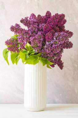 Beyaz bir vazoda bir demet leylak çiçeği macun efektli pembe bir duvarın arka planında..