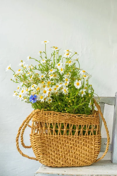 A bouquet of field daisies in a wicker vintage bag in a vintage interior against a white wall.