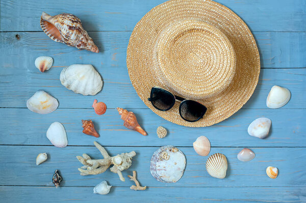 Straw hat, sunglasses and seashells on a blue wooden background. Marine holiday concept.
