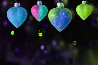 Çok renkli ışıklar ve bokeh 'li koyu bir arka planda bir dizi kalp şeklinde Noel oyuncağı. Yeni yıl arkaplanı.