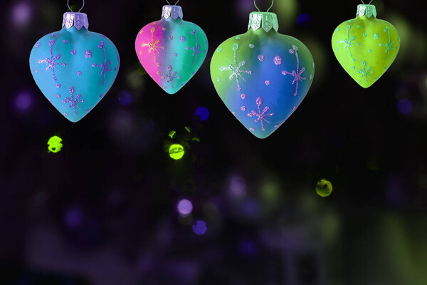 a row of multi-colored heart-shaped Christmas toys on a dark background with multi-colored lights and bokeh.  christmas new year background.
