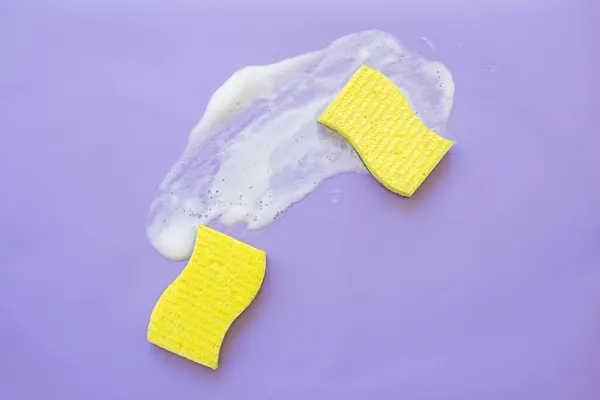 Cleaning supplies - sponge and cleaning agent on a lilac background. Flat lay, top view, copy space