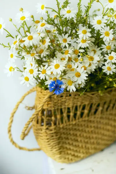 a bouquet of field daisies and cornflowers in a vintage wicker bag on a light background.