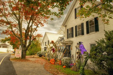 Parlayan Cadılar Bayramı süslemeleri. İskeletler, cadılar, evin etrafında balkabakları. Renkli sonbahar ağaçları,