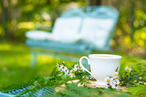 A cup of tea or coffee on a table in the garden and a cozy sofa with pillows in the background. Wonderful summer holiday