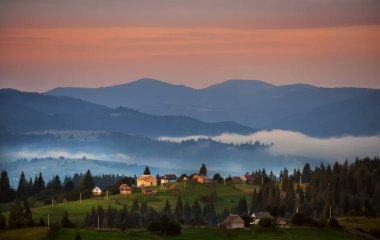 Sabahın erken saatlerinde dağlarda küçük bir köy manzarası. Dağların siluetleri ve vadideki sis