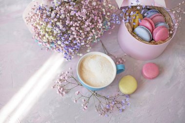  Tatlı renkli badem kurabiyeleri, sevimli renkli çiçekler ve açık pembe arka planda sütlü bir fincan kahve. Kutlama ve romantizm atmosferi