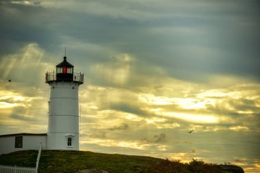 Deniz feneri Nubble 'ın dramatik bir arka planı var. Güneş ışınları ve gökyüzünde kuşlar var. ABD. Maine. New England Seacoast.