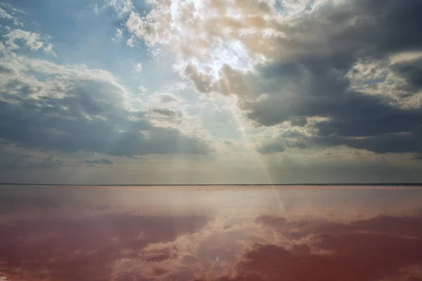 Salt lake with rose water and salt. Magnificent landscape of a salt lake on a sunny day. Dramatic sky with sun rays.